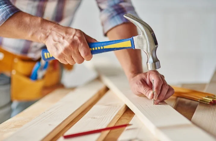 Person hämmert einen Nagel in ein Holzbrett